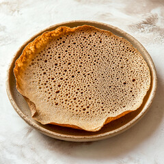 a traditional Ethiopian dish, served on a round ceramic plate with a neutral background, showcasing its spongy texture and cultural significance