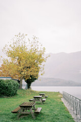 Wooden benches and tables stand on a green lawn near Lake Como. Italy