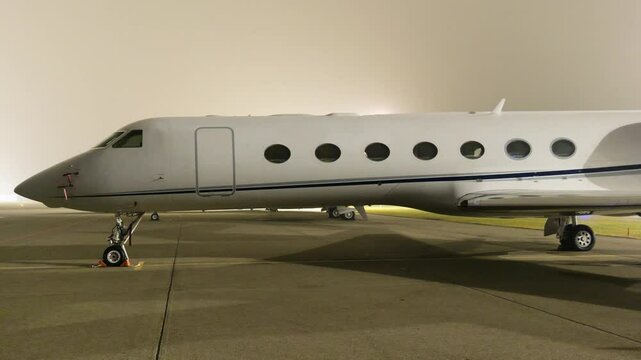 white heavy business jet parked apron fbo gat stands private aircraft emphasized during dark night airport close up panning shot area 