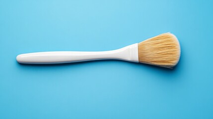 White handled brush with light brown bristles on a light blue background. Simple, clean studio shot