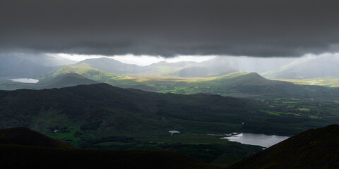 A breathtaking panorama of lush green hills and mountains, illuminated by rays of sunlight breaking...