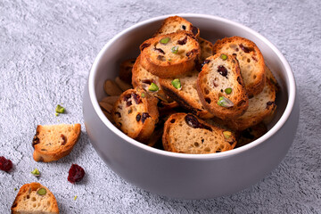 Rusks with dried cranberries and pistachios in a ceramic bowl on a gray background