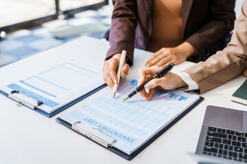 Two female business professionals in suits sit at desk, engaged in strategic discussion. They analyze financial planning, risk management, corporate growth while reviewing reports and market trends.