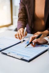 Two female business professionals in suits sit at desk, engaged in strategic discussion. They...