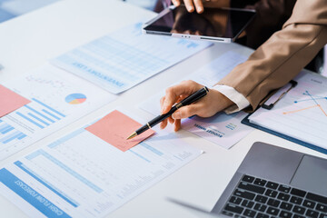 Two female business professionals in suits sit at desk, engaged in strategic discussion. They...