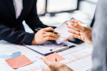 Two female business professionals in suits sit at desk, engaged in strategic discussion. They...