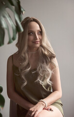 An elegant blonde girl in a thin dress sits on a chair in a minimalist interior.