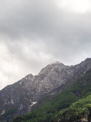 Naklejka premium A towering mountain peak with rugged rock formations and patches of greenery, partially covered by clouds. The overcast sky adds a dramatic and moody atmosphere to the scene.