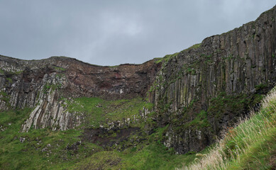 A cliff wall at Giant's Causeway, Ireland, featuring tall basalt columns under an overcast sky, showcasing natural geological formations