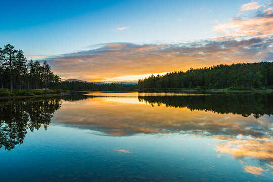 Sunset over serene lake in Sweden reflecting vibrant colors of nature and surrounding trees