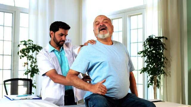Indian Asian male physiotherapist examining senior retired patient with chronic back pain in a lavish clinic, ensuring precise diagnosis and effective rehabilitation for pain relief and improved mobil