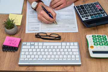 man filling Polish tax form with pen calculator laptop at home. Finance, tax income concept