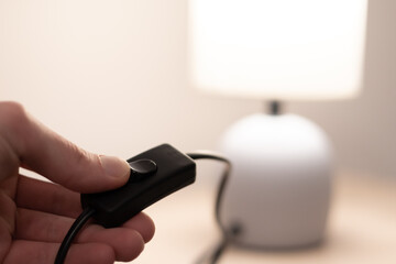 People is turning on modern night table lamp switch. Warm lighting for bedside lamp for reading books. Close up.