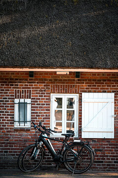 Two bicycles lean against a small brick house with a thatched roof.