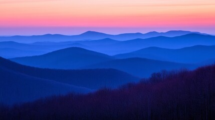 Blue and purple hues paint the evening sky over a vast mountain range. Layers of silhouettes stretch to the horizon, creating a tranquil, serene landscape.