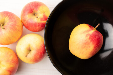 Several juicy apples with a ceramic plate on a wooden table, close-up, top view.
