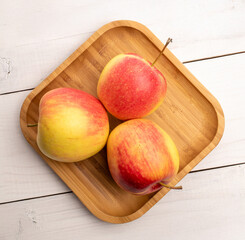 Three juicy apples with bamboo plate on wooden table, close-up, top view.