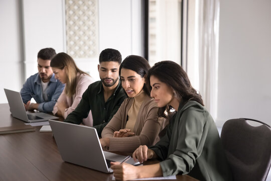 Group of focused workmates looking at laptop screen, watching content related to their workflow, review new software, considering details, working together on online presentation gathered in coworking