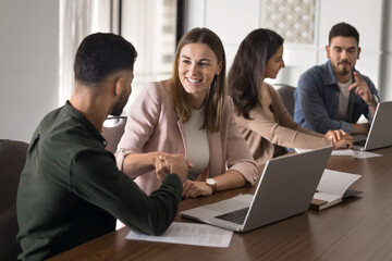 Two teammates greeting each other before teamwork met in co-working space seated at desk with...