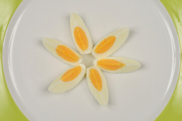 A top-down shot of six hard-boiled egg slices arranged in a circular pattern on a white plate with a green rim