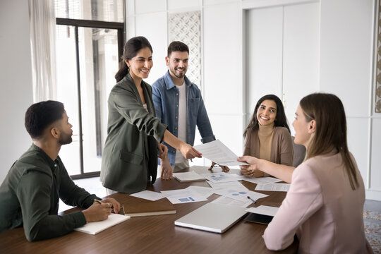 Group of professionals gathered around conference table, collaborating on project, female boss handing over document to client or colleague, engaged in data analysis or strategic planning in boardroom