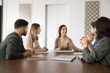 Professional team engaged in collaborative discussion around conference table, listening speech of confident Latina boss sharing ideas, leading formal meeting, providing project details and feedback