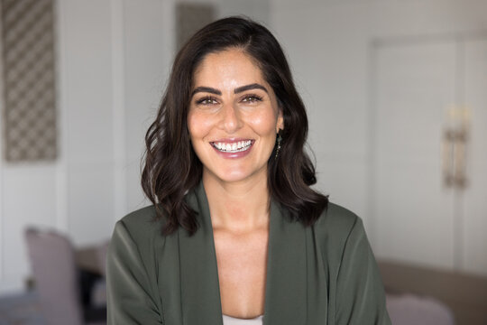 Head shot portrait of beautiful laughing Mexican businesswoman dressed in formal attire, standing in workspace, look at camera with joyful expression, exuding professionalism, independence and success