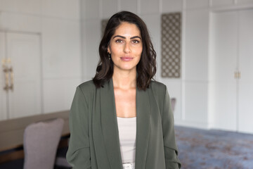 Confident serious Hispanic businesswoman, coach or CEO standing alone in modern boardroom of...