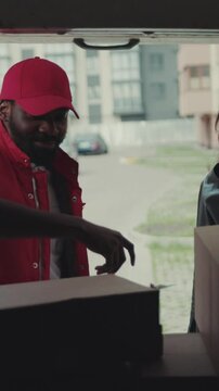 Courier African American gives a parce to a smiling woman after signing on delivery device cardboard technology box order post postal service device sunny beard covered load logistic mailman