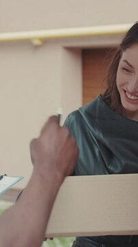 Smiling courier African American gives a parce to a woman after signing on delivery device cardboard technology box order post postal service device sunny beard covered load logistic mailman