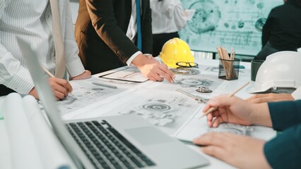 A diverse technical team engages in collaboration over blueprints and a laptop, showcasing a modern office environment filled with creativity and strategic planning. SACTR