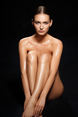 Fototapeta premium Model poses gracefully with crossed legs in a minimalist studio setting, showcasing smooth skin and serene expression