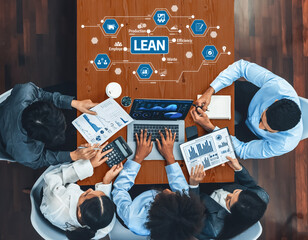A diverse team collaborates over data analysis, discussing lean principles and efficiency strategies at a modern office workspace, highlighting productivity and teamwork. Amity