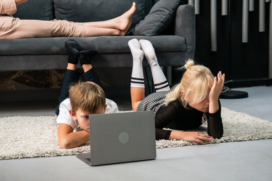 Kids Laptop Home - Two children using a laptop while lying on the floor in a living room.