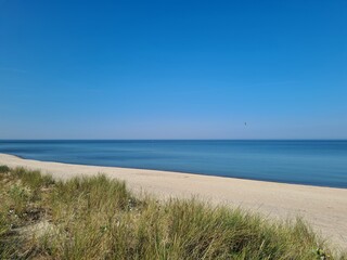 Spokojna piaszczysta plaża nad Morzem Bałtyckim, z błękitną wodą, czystym niebem i nadmorskimi wydmami porośniętymi trawami, letni krajobraz.