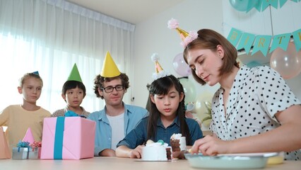 Caucasian mother cutting cake while family congratulate in girl's birthday. Diverse family celebrate daughter important day while waiting for eating dessert and food while smiling together. Pedagogy.