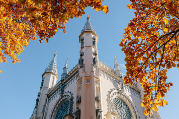 View of the spire of the church in the medieval Gothic style in the autumn park, the tops of the towers. Gothic chapel. Autumn
