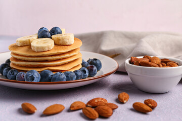Plate with sweet pancakes, banana, blueberry and nuts on pink background, closeup