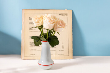 Moscow, Russia - February 23, 2025. A bouquet of delicate pink roses in a white ceramic vase on a blue background with a white vinyl cover and a white table. Space for text. Bridal wedding bouquet.