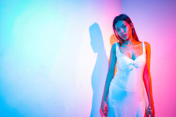 Fototapeta premium female model with long hair wearing a long white dress with a slit with a blue and red background