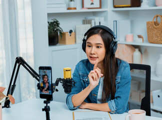 Host channel Asian influencer talking in broadcast wearing headsets on social media live on smartphone recording online, greeting listeners with coaching life or business at modern studio. Stratagem.
