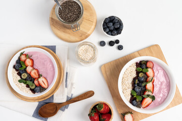 Presented by fruits putting yogurt toppings with strawberry, berry, oats, raisins and chia seed decorated by peppermint in white blow. Pink background. Set of healthy dairy product choice. Pecuniary.