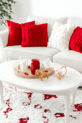 Festive decor on a white coffee table with candles ornaments and red accents  Cozy white sofa with red pillows in bac