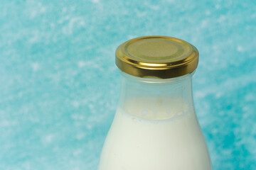 Glass milk bottle with a golden cap, placed against a soft blue background. The image evokes freshness, simplicity, and classic charm, perfect for themes of dairy products or home comfort.