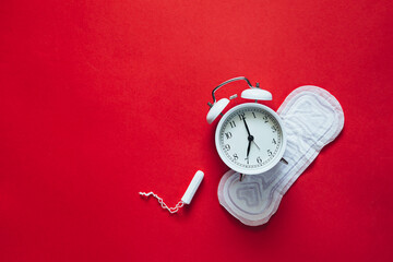 Hygienic female pad with tampon and alarm clock on red background, flat lay.