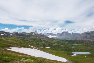 Scenic awesome landscape with big snowfield and alpine lake among green hills and rocks with view...