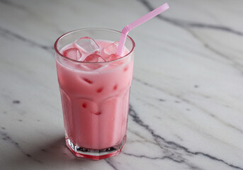 A pink glass of air bandung (rose syrup with milk) served with ice cubes and a straw. The drink is placed on a marble surface