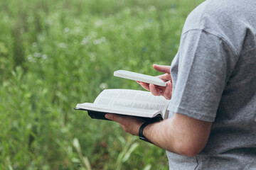A man with a smart phone and a Bible in his hands outside.
