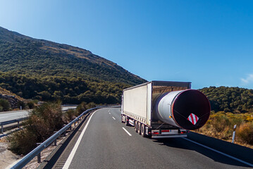 Truck transporting a huge pipe that protrudes from the back of the vehicle, oversized cargo.