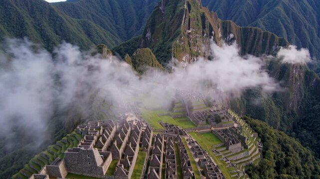 Low clouds are moving across the ancient inca city of machu picchu, located high in the andes mountains of peru, creating a mystical atmosphere